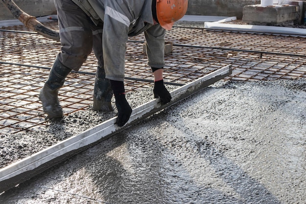 Der Arbeiter nivelliert den Beton in der Regel beim Gießen des Bodens auf der Baustelle.