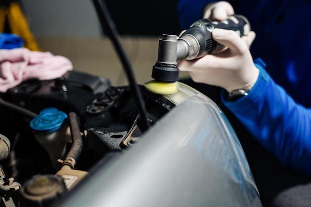Der Arbeiter poliert Optiken von Scheinwerfern des Autos mit dem Elektrowerkzeug