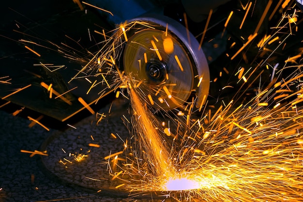 Der Arbeiter schneidet ein Blech mit einer Schleifmaschine Fliegen Sie helle Funken Arbeitsprozess in der Werkstatt in der Fabrik