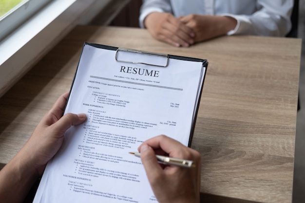 Foto der arbeitgeber, der einen jungen männlichen arbeitssuchenden interviewt, der an einem tisch sitzt und seinen lebenslauf liest, sah herauf