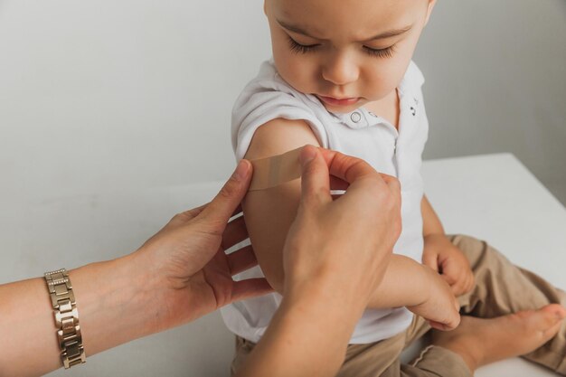 Der Arzt bringt dem Kind ein Pflaster auf die Schulter, nachdem er den Impfstoff mit einer Spritze injiziert hat. Der Patient erhält Erste Hilfe. Nahansicht. Impfung für Kinder.