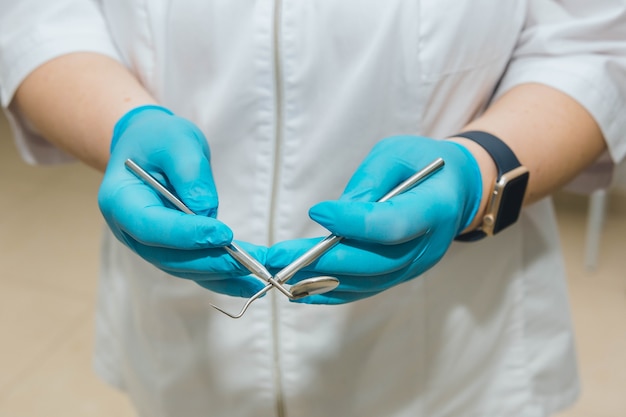 Der Arzt hält das Instrument in den Händen Blaue Handschuhe an den Händen des Zahnarztes