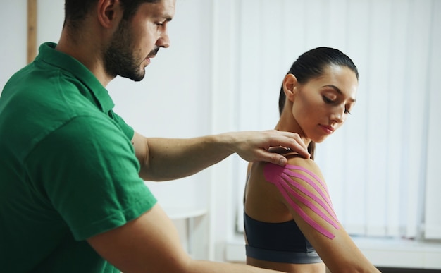 Der Arzt hilft der Frau bei der Schulterbehandlung mit Kinesio-Tape.