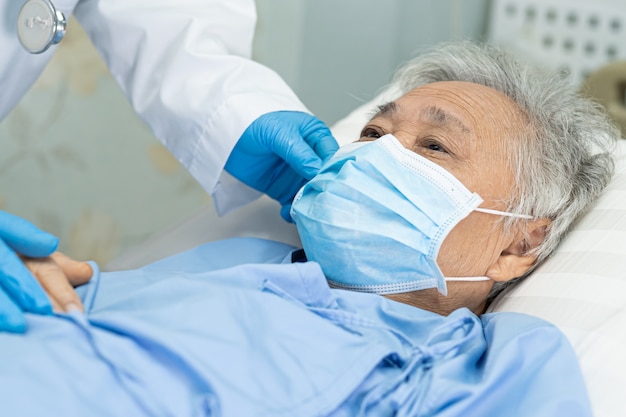Der Arzt hilft einer asiatischen älteren Patientin, die im Krankenhaus eine Gesichtsmaske trägt, um das Covid-19-Virus zu schützen.