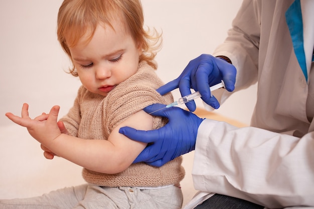Der Arzt impft das Kind gegen Coronavirus. Das Kind hat keine Angst vor Impfungen und ist ruhig. Ein Mann in Robe, Hut, Maske und Handschuhen spritzt dem Kind. Heimquarantäne, Covid.