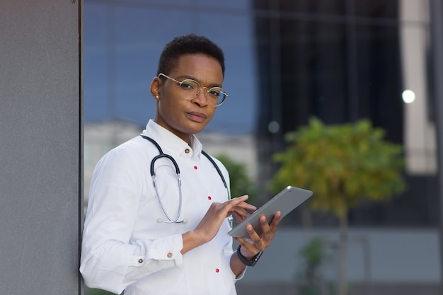 Der Arzt in der Nähe der Klinik hält einen Tablet-Computer in der Hand, liest die Nachrichten Afroamerikaner studiert ernsthaft Informationen aus dem Internet, für Online-Konsultationen mit Patienten