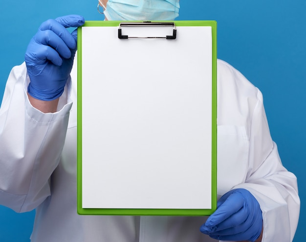 Der Arzt in einem weißen Gewand mit blauen medizinischen Handschuhen hält einen Ordner mit sauberen weißen Laken