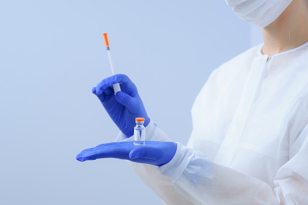 Der Arzt in medizinischen Handschuhen und einer Maske hält einen Impfstoff in den Händen