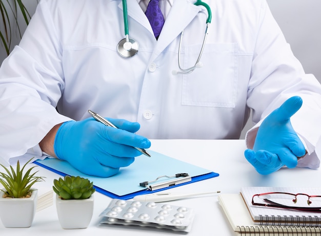 Der Arzt in weißer Uniform sitzt an einem weißen Tisch und schreibt mit sterilen Handschuhen an den Händen in ein Notizbuch