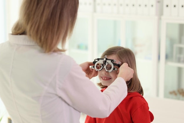 Der Arzt setzt einem kleinen Mädchen eine Augenschutzbrille auf, um die Sehkraft einer Frau in medizinischer Uniform zu überprüfen