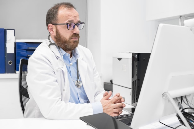 Der Arzt spricht mit dem Online-Patienten auf dem Desktop-Computerbildschirm, der am Schreibtisch der Klinik sitzt und eine Online-Beratung für die häusliche Gesundheitsbehandlung gibt Telemedizin Fernarzttermin