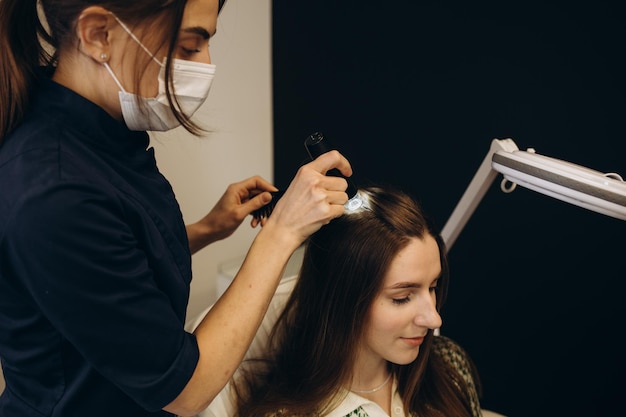 Der Arzt Trichologe untersucht die Haare der Patientin mit einem Trichoskop in der Klinik Verfahren der Trichoskopie Haare Läuft ein Trichoskop über die Kopfhaut und sieht das Ergebnis auf dem Bildschirm aus Computer-Trichoskopie