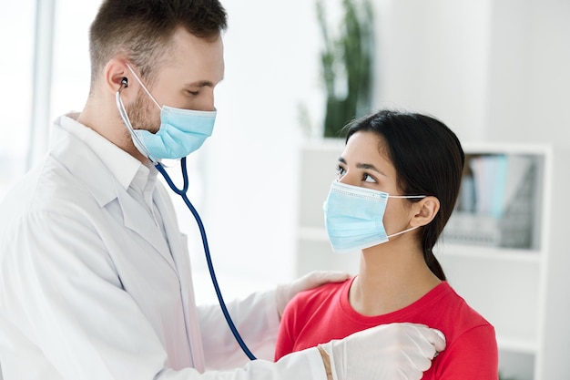 Der Arzt untersucht die Gesundheit einer Frau mit medizinischer Maske, rotem T-Shirt und Stethoskop