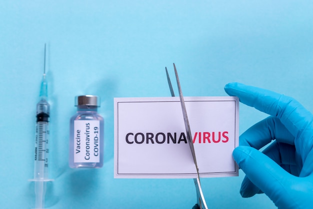 Der Arzt verwendet eine Schere, die das Wort "Virus" aus dem Text "Coronavirus" über dem Hintergrund des Impfstoffs und der Spritze schneidet