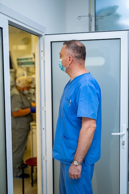 Der Arzt wird einen modernen Operationssaal betreten. Sanitäter in Peelings und Maske, halb zur Kamera gedreht. Nahaufnahme.