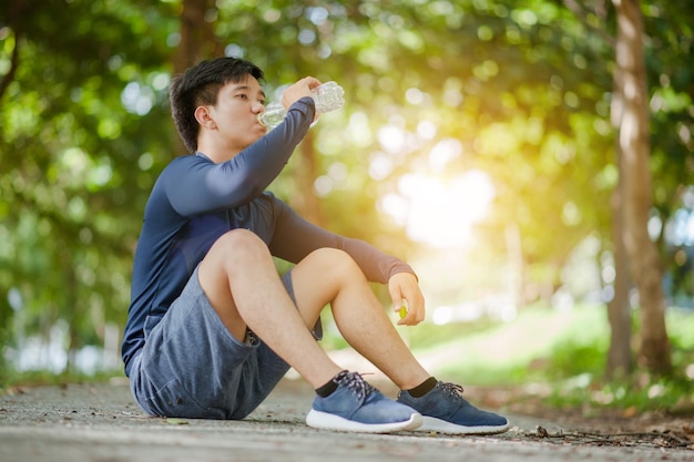 Der Asiate trinkt Wasser aus einer Flasche, nachdem er im Park gelaufen ist