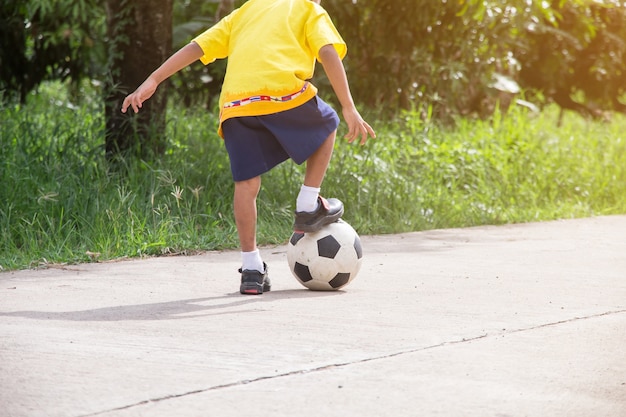 Der asiatische junge, der alten fußball auf straße spielt, spielen fußball für übung am abend