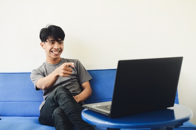 Der asiatische Mann auf dem Sofa zeigte auf den Laptop