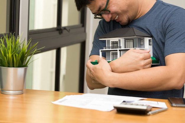 Der asiatische Mann, der ein Traumhaus lächelt und umarmt und berechnet, um ein Haus zu kaufen, das an seiner Zukunft träumt