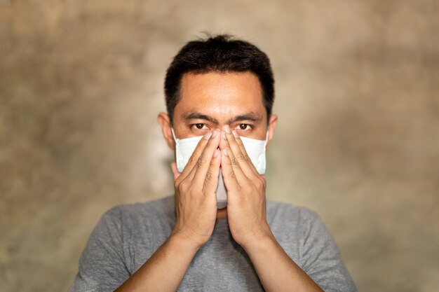 Der asiatische Mann, der eine Gesichtsmaske mit der Hand trägt, bedecken seinen Mund beim Husten.