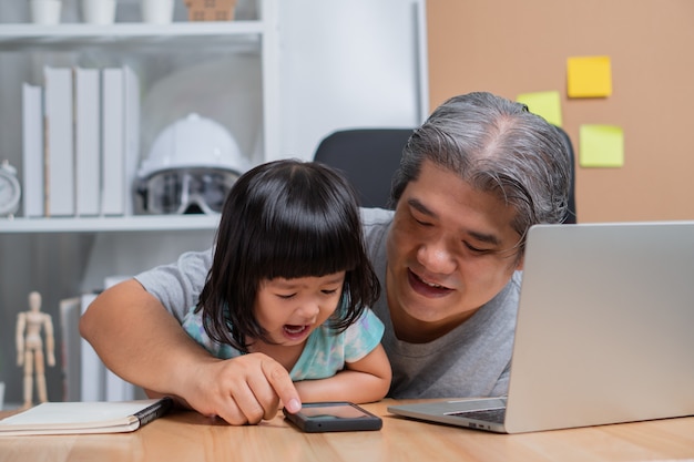 Der asiatische Vater arbeitet zu Hause mit einer Tochter und lernt gemeinsam Online-Lernen von der Schule.