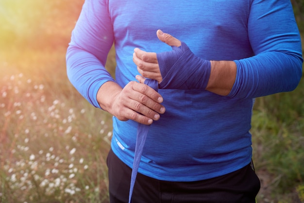 Der Athlet steht und umwickelt seine Hände mit einem blauen Textilverband