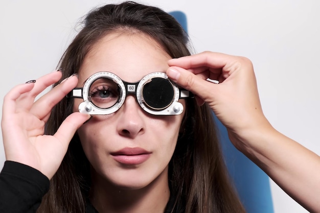 Der aufmerksame Optometrist untersucht eine schöne Patientin, die ihr Sehvermögen in einer Augenklinik überprüft Der Arzt fügt eine schwarze Linse in einen Proberahmen ein Untersuchung in einer modernen Klinik