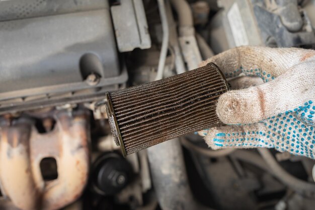 Der Automechaniker hält einen alten Ölfilter in der Hand, der durch einen neuen ersetzt werden soll