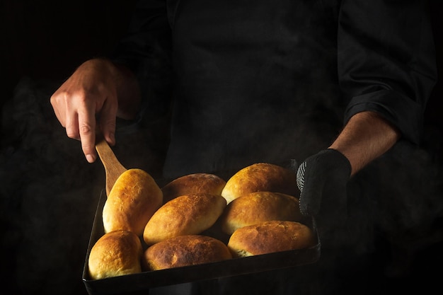 Der Bäcker backt Kuchen oder Hot-Dog-Brötchen auf einem heißen Backblech Schwarzer Platz für Menü oder Rezept