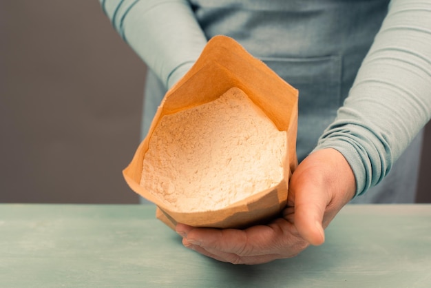 Der Bäcker hält eine Papiertüte mit weißer Weizenmehl-Backzutat für Brot, Pizza oder Gebäck