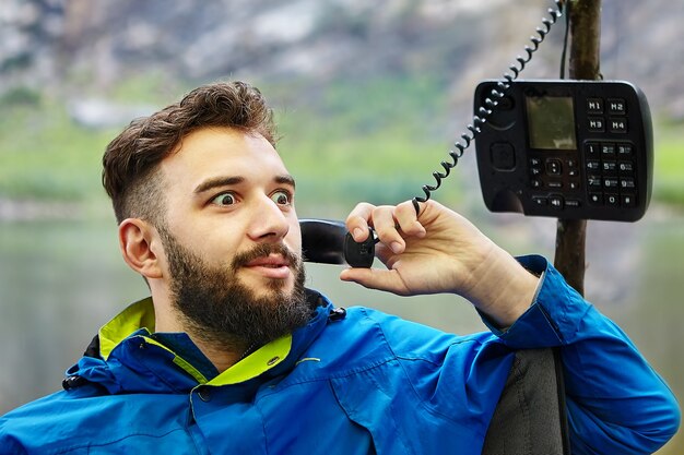 Der bärtige kaukasische Mann spricht über ein Drucktastentelefon eines veralteten Modells mit einer Röhre auf einem verdrillten Draht.