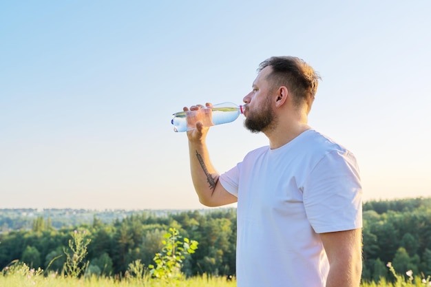 Der bärtige Mann mittleren Alters trinkt an heißen Sommertagen Wasser aus der Flasche
