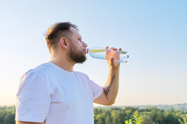 Der bärtige Mann mittleren Alters trinkt an heißen Sommertagen Wasser aus der Flasche