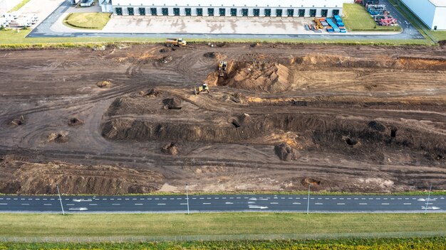 Der Bagger gräbt einen Graben unter das Fundament und der Bulldozer räumt den Boden. Draufsicht auf eine Baustelle