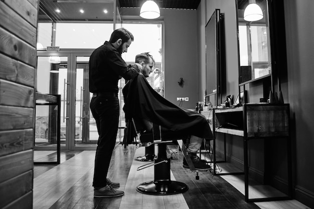 Der Barbier, ein Mann mit Bart, der gerade einen Kunden im Friseursalon schneidet, ein Schwarz-Weiß-Foto