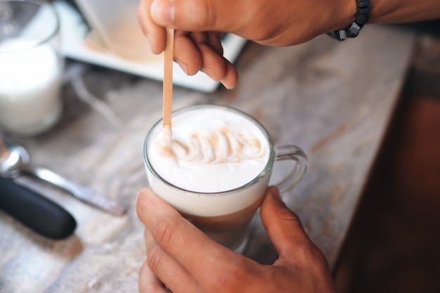 Der Barista zeichnet ein Muster auf den Schaum eines Cappuccinos