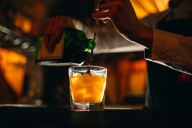 Der Barkeeper bereitet an der Bar einen Cocktail zu. Der Barkeeper gießt Alkohol aus einer Flasche