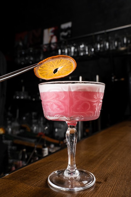 Der Barkeeper dekoriert den alkoholischen Cocktail des rosafarbenen Clover Clubs mit einer Orangenscheibe an der Bar. Der Barkeeper mischt trockenen Wermut aus Eiweiß und Zitrone und Gin, um den Clover Club-Cocktail zuzubereiten