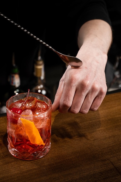 Der Barkeeper gibt einen Tropfen alkoholischen Negroni-Cocktails auf seine Hand und probiert ihn. Der Barmann bereitet an der Bar einen klassischen Negroni-Cocktail zu