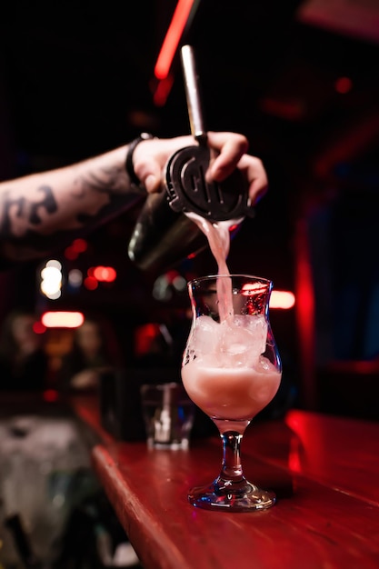 Der Barkeeper gießt den fertigen Cocktail vorsichtig aus dem Shaker in ein Glas