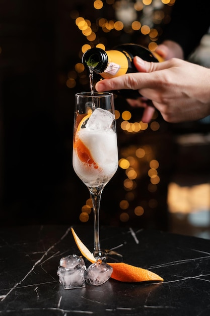 Der Barkeeper gießt Sekt in ein Glas mit Eis und Orangenschale