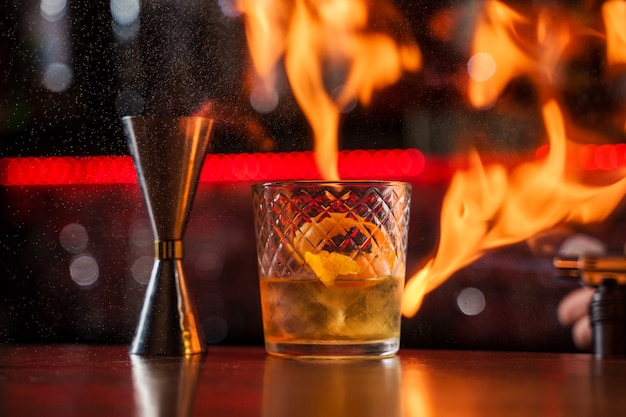 Der Barkeeper macht Flamme über einem Cocktail mit Orangenschale aus nächster Nähe.