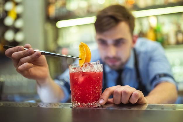 Der Barmann macht einen Cocktail mit einer Orange an der Bar