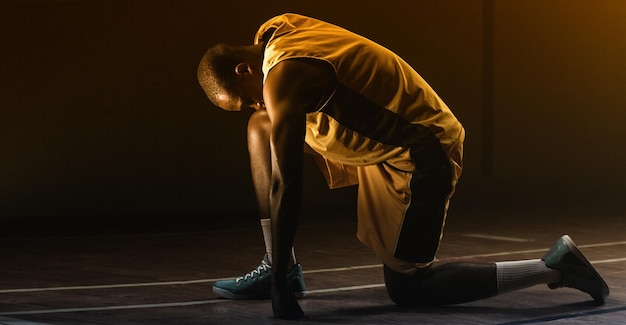 Der Basketball-Spieler, der sich vorbereitet, mit dem Knie auf dem Boden und dem Kopf zu spielen, senkte sich