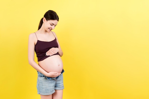 Der Bauch der nackten schwangeren Frau trägt geöffnete Jeans auf buntem Hintergrund mit Kopierbereich Schwangerschaftskonzept