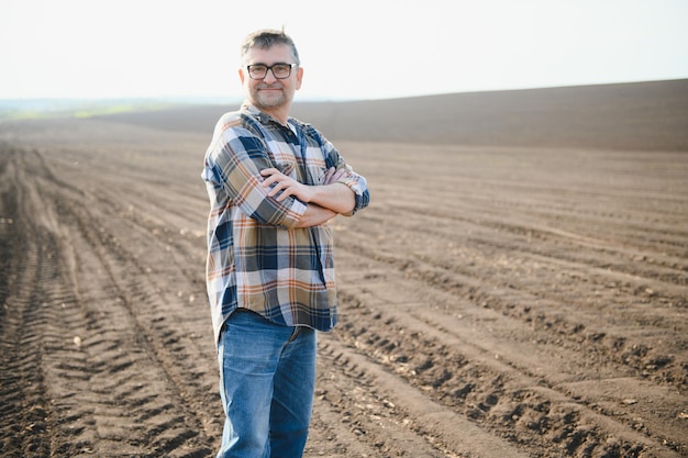 Der Bauer arbeitet auf dem Boden. Männlicher Bauer auf einem gepflügten Feld, der im Frühjahr Getreide in den Boden pflanzt. Landwirtschaftliches Geschäftskonzept. Anbau von Nahrungsmittelgemüse