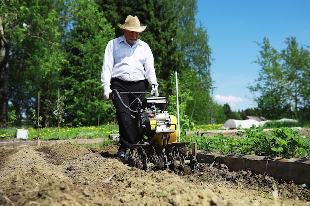 Der Bauer gräbt einen Garten um Ein Mann mit einem Mähdrescher pflügt den Garten Der grauhaarige Großvater mäht den Garten