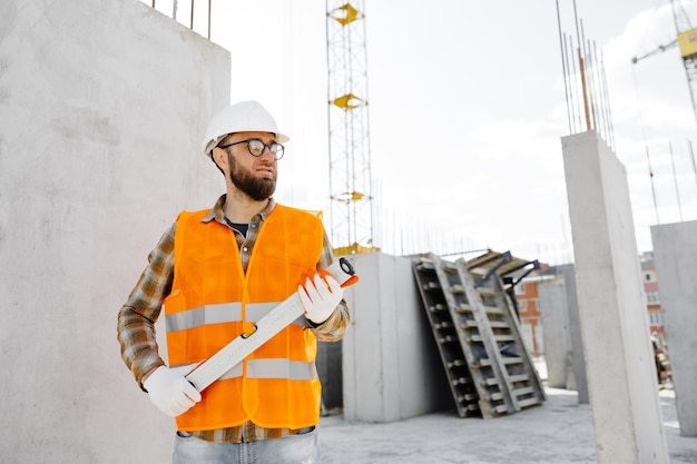 Der Baumeister mit Schutzhelm und Weste steht am Arbeitsplatz im Gebäude und hält das Lineal in den Händen