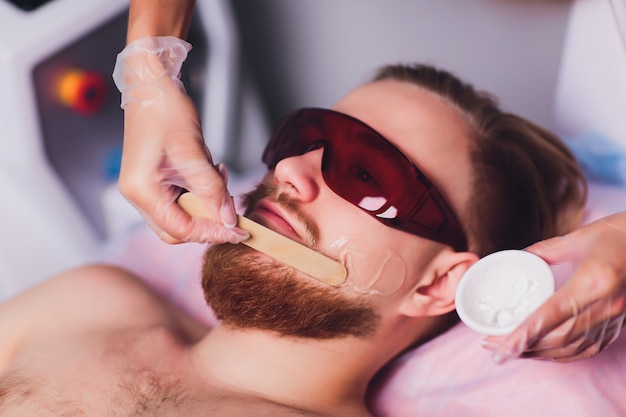 Der behandelnde Arzt entfernt permanent unerwünschte Gesichtshaare bei einem bärtigen Mann mit einem Laser. Schönheit und Gesundheit.
