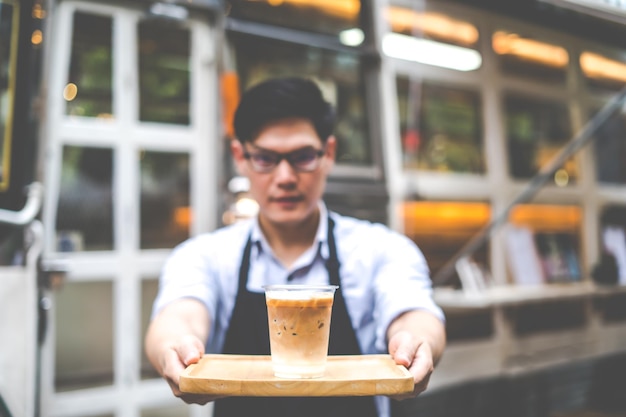 Der Besitzer eines kleinen Cafés begrüßt seine Kunden vor dem Café mit einem Lächeln und einer Tasse Kaffee in der Hand. KMU-Geschäftsinhaber-Konzept. Konzentriere dich auf die Kaffeetasse